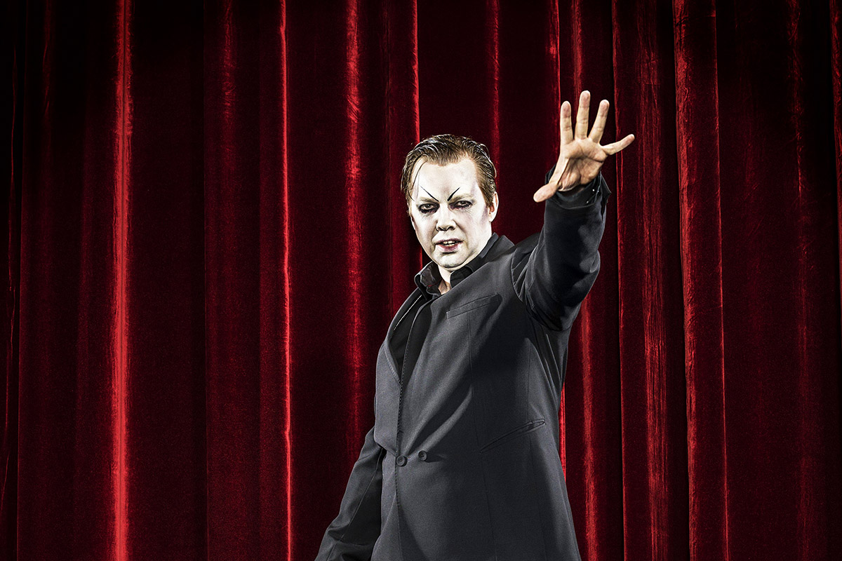 kampanjbild Mephisto, Fredrik Everssträcker ut armen stående framför röd ridå