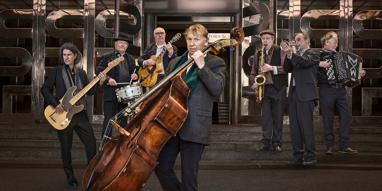 Framför huvudentrén till Göteborgs Stadsteater: I förgrunden Tomas von Brömssen. I bakgrunden Michael Krönlein, Per Melin, Anders Blad, Stefan Sandberg, Daniel Ekborg, Bernt Andersson- alla med olika musikinstrument.